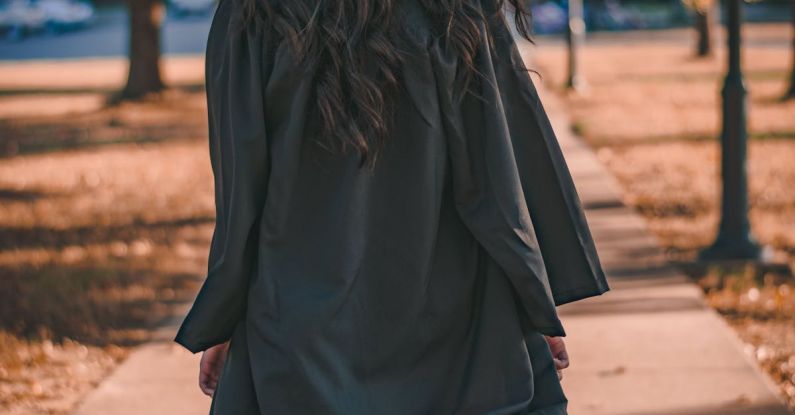 Graduation Cap - Woman in Black Long Sleeve Dress Standing on Brown Concrete Pathway