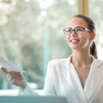 Confidence Booster - Low angle of successful female executive manager in classy style sitting at table with laptop in contemporary workplace and passing documents to colleague