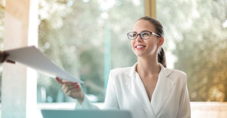 Confidence Booster - Low angle of successful female executive manager in classy style sitting at table with laptop in contemporary workplace and passing documents to colleague