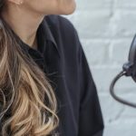 Interview Outfit - Glad female with long wavy hair in black shirt talking while recording voice in modern studio with brick walls