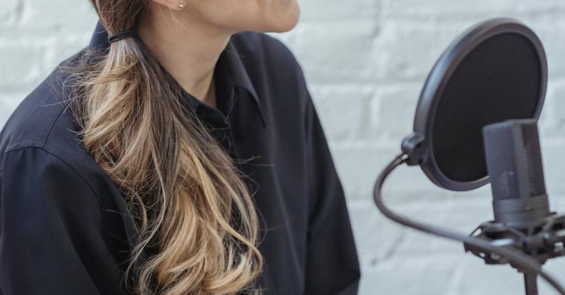 Interview Outfit - Glad female with long wavy hair in black shirt talking while recording voice in modern studio with brick walls