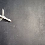 Global Shipping - Top view of crop anonymous person driving toy airplane on empty blackboard while representing journey concept