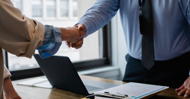 Lease Contract - Crop unrecognizable coworkers in formal wear standing at table with laptop and documents while greeting each other before meeting