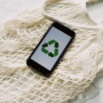 Recycle Symbol - Overhead of smartphone with simple recycling sign on screen placed on white eco friendly mesh bag on marble table in room