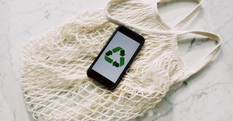 Recycle Symbol - Overhead of smartphone with simple recycling sign on screen placed on white eco friendly mesh bag on marble table in room